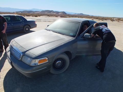 2003 Ford Crown Victoria - Person reaches into the open door of a gray Crown Victoria with steel wheels on a dry lakebed