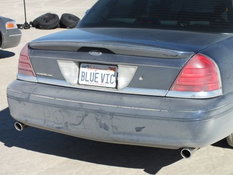 2003 Ford Crown Victoria - Close rear of a gray Crown Victoria LX, BLUE VIC California plate, POLICE drawn in dust on bumper