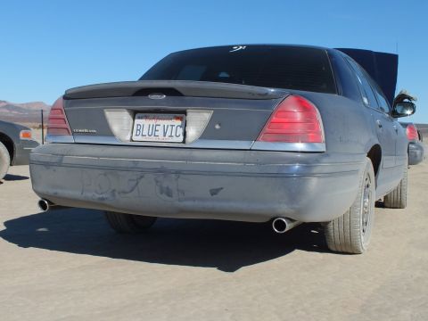 2003 Ford Crown Victoria - Dual exhaust tips and a BLUE VIC plate mark this Crown Victoria parked on cracked desert ground.