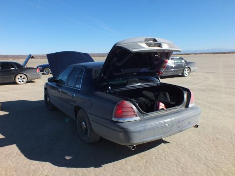 2003 Ford Crown Victoria - Black Crown Victoria opened front and rear reveals an empty trunk, parked among sedans on the playa.