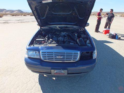 2003 Ford Crown Victoria - Blue Crown Victoria front end with hood up and Ford oval grille; two men stand at a cooler behind.