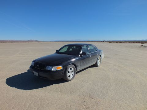 2003 Ford Crown Victoria - Black Crown Victoria with alloy wheels sits alone on the cracked playa with distant mountains.