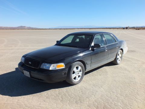2003 Ford Crown Victoria - Black Crown Victoria angled across the lakebed, Ford grille badge and amber markers visible.
