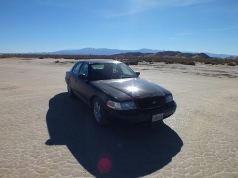 2003 Ford Crown Victoria - Sun glints off a black Crown Victoria parked on the playa before distant snow-dusted peaks.