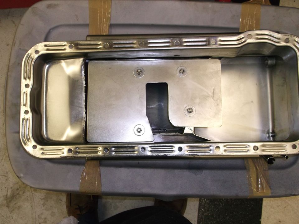 Oil pan with a metal baffle installed inside, sitting on a gray plastic tub