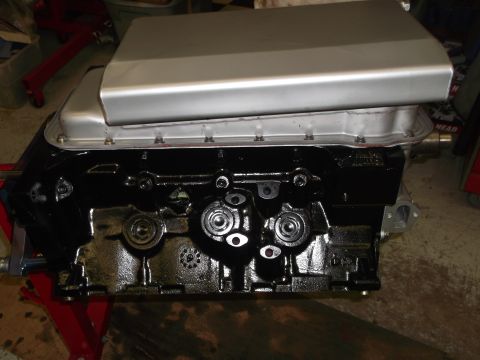 1965 Shelby Cobra - A black engine block with a silver valve cover is shown, mounted on a red engine stand.