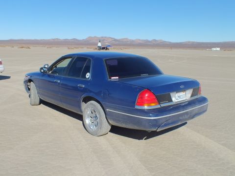 2003 Ford Crown Victoria - Dark blue Crown Victoria with chrome wheels parked on the playa, Ford oval on the trunk lid.