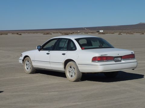 2003 Ford Crown Victoria - White Crown Victoria angled on the playa, taillights and trunk badging facing the camera.