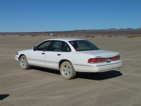 2003 Ford Crown Victoria - White Crown Victoria with alloy wheels parked on the cracked playa under a clear blue sky.