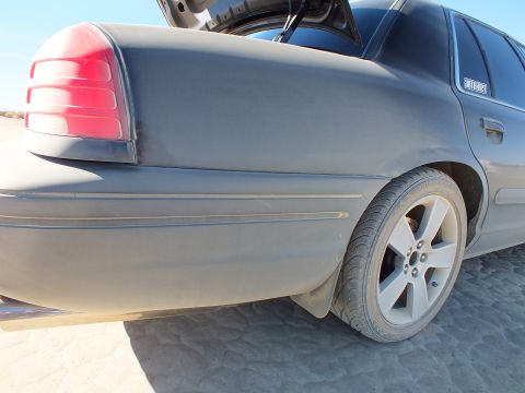 2003 Ford Crown Victoria - Close rear corner of a matte gray full-size sedan, taillight and alloy wheel in desert light.