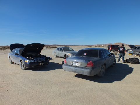 2003 Ford Crown Victoria - Three sedans spread across cracked desert flats, hoods raised, a person changing a tire.