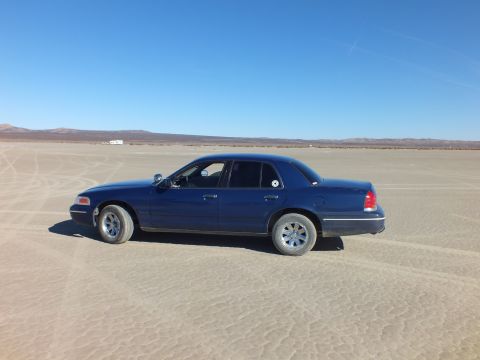 2003 Ford Crown Victoria - Side profile of a dark blue sedan alone on cracked playa with low mountains behind.