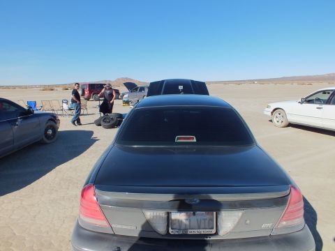 2003 Ford Crown Victoria - Tail view of a Ford sedan, Crown Victoria plate frame, people and cars across the playa.
