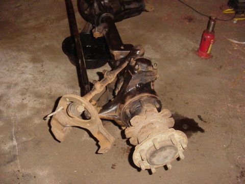 1992 Ford Bronco - Front axle assembly, likely from a truck or SUV, is shown disassembled on a garage floor.
