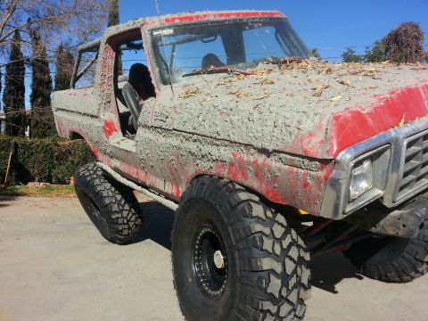 1978 Ford Bronco - This heavily modified 1978 Ford Bronco is caked in mud and debris, obscuring its original red paint.