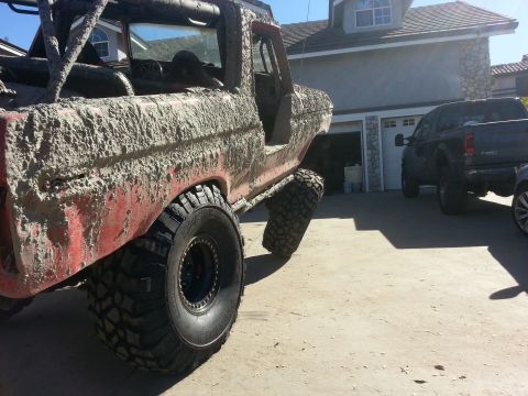 1978 Ford Bronco - This heavily modified off-road vehicle is covered in mud, with another pickup truck visible in the background.