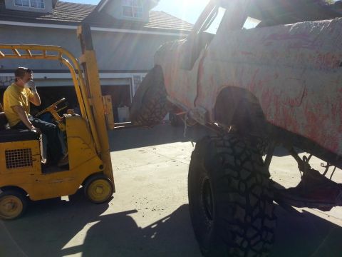 1978 Ford Bronco - A forklift lifts a heavily modified off-road vehicle covered in mud.