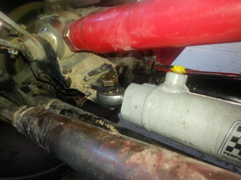 1978 Ford Bronco - Close-up view of vehicle suspension components, showing a red tube and a grey cylinder.