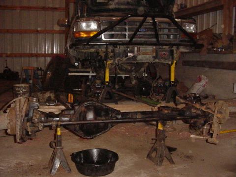 1992 Ford Bronco - The front axle and suspension components of a 1992 Ford Bronco are disassembled and supported by jack stands in a garage.