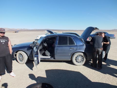 2003 Ford Crown Victoria - Side of a blue full-size sedan, front door and hood open, two people working under hood.