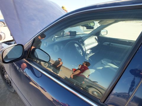 2003 Ford Crown Victoria - View through a blue sedan window into the dash and gauges, people reflected on the glass.