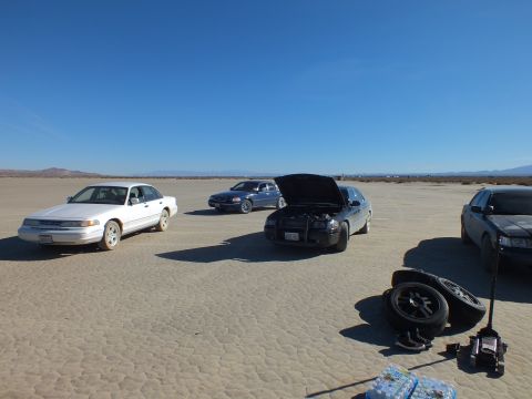 2003 Ford Crown Victoria - Four full-size sedans gathered on cracked desert flats, a spare wheel and floor jack staged nearby