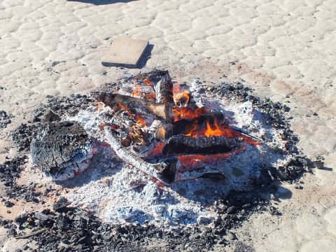 2003 Ford Crown Victoria - Flames rising from charred logs surrounded by a wide ring of ash on desert flats