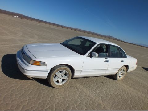 2003 Ford Crown Victoria - White full-size Ford sedan with aftermarket wheels sits on cracked desert flats