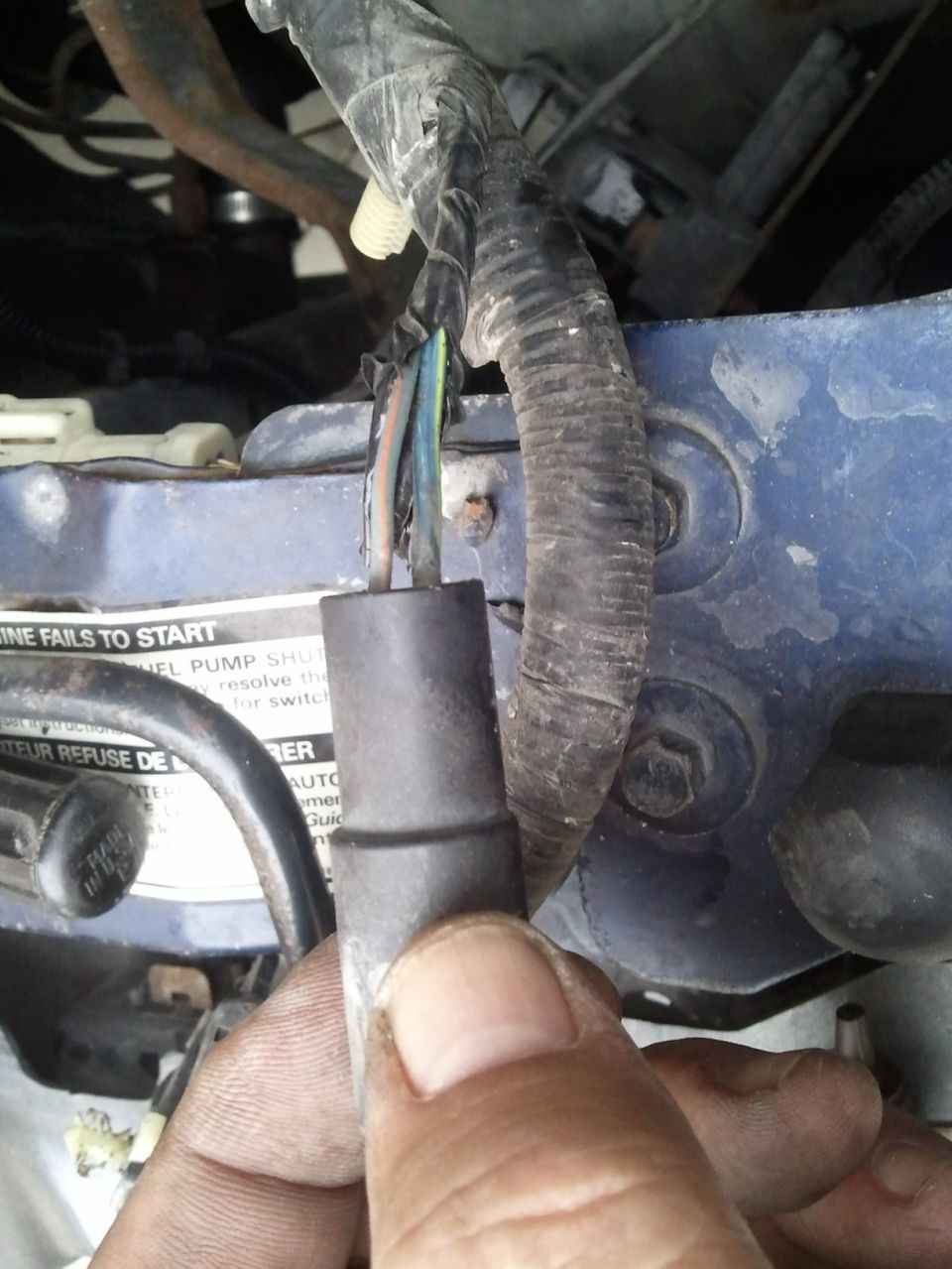 Hand holding engine wiring harness connector with wires exposed