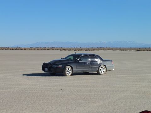 2003 Ford Crown Victoria - Black sedan on cracked desert lakebed beneath clear sky with a distant mountain range