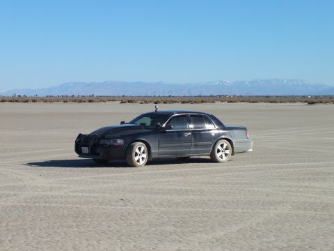 2003 Ford Crown Victoria - Side view of a black full-size Mercury sedan on cracked desert flats near distant peaks