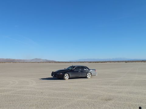 2003 Ford Crown Victoria - Black full-size sedan on cracked desert flats beneath a wide sky and far mountain range
