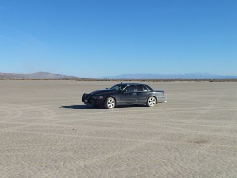 2003 Ford Crown Victoria - Black full-size Mercury sedan on cracked desert flats beneath clear sky near far peaks