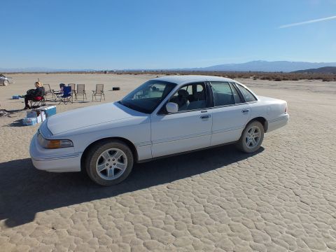 2003 Ford Crown Victoria - Side view of a white full-size sedan with alloy wheels parked on cracked playa terrain.