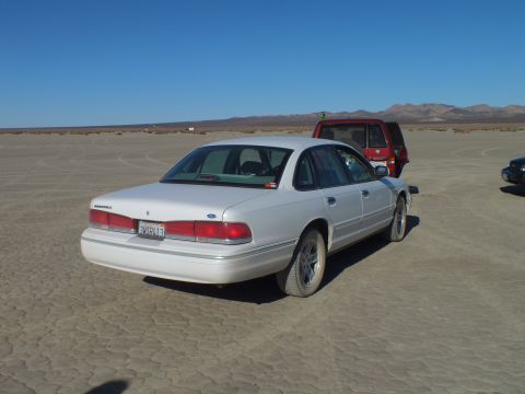 2003 Ford Crown Victoria - Rear of a white Ford sedan showing taillights and a California plate, red SUV to the side.