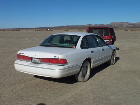 2003 Ford Crown Victoria - Rear three-quarter view of a white Ford sedan with California plate parked on cracked playa.