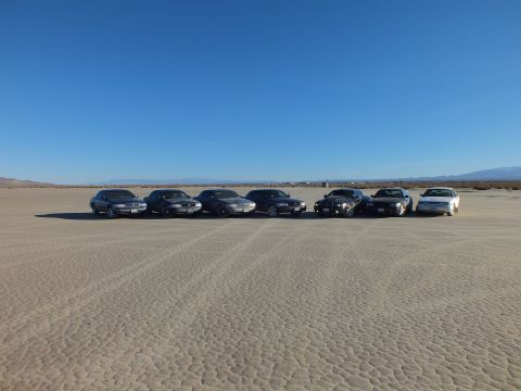 2003 Ford Crown Victoria - Front-facing lineup of seven sedans on dry playa, distant ranges across the horizon.