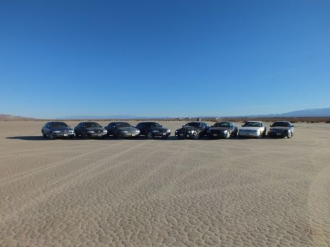 2003 Ford Crown Victoria - Eight sedans parked side by side on cracked playa with distant snowy mountains.