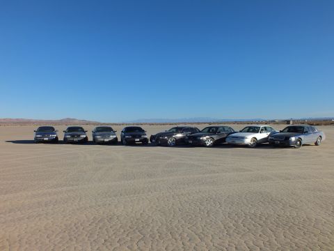 2003 Ford Crown Victoria - Eight sedans staggered across cracked playa with mountains far on the horizon.