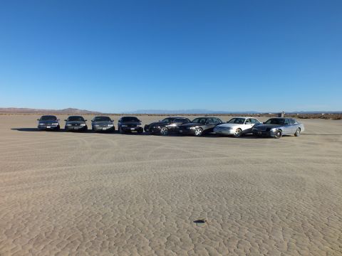 2003 Ford Crown Victoria - Front view of eight sedans parked side by side on dry playa, hills in the distance.
