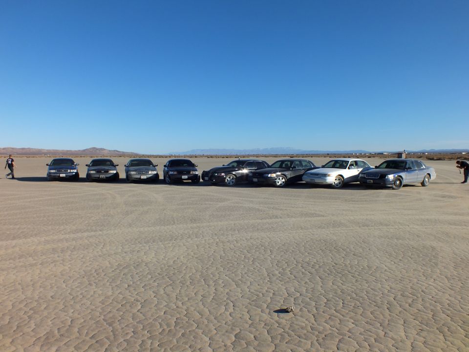 Eight sedans lined up on a desert lakebed with two people standing at either end