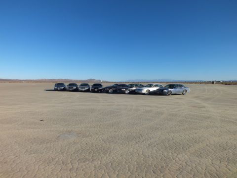 2003 Ford Crown Victoria - Staggered lineup of eight sedans on cracked playa with tire tracks across the flats.