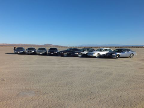 2003 Ford Crown Victoria - Lineup of sedans on cracked playa with distant mountains and clear blue sky