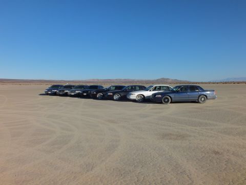 2003 Ford Crown Victoria - Full-size sedans staged on a lakebed with mountains on the horizon
