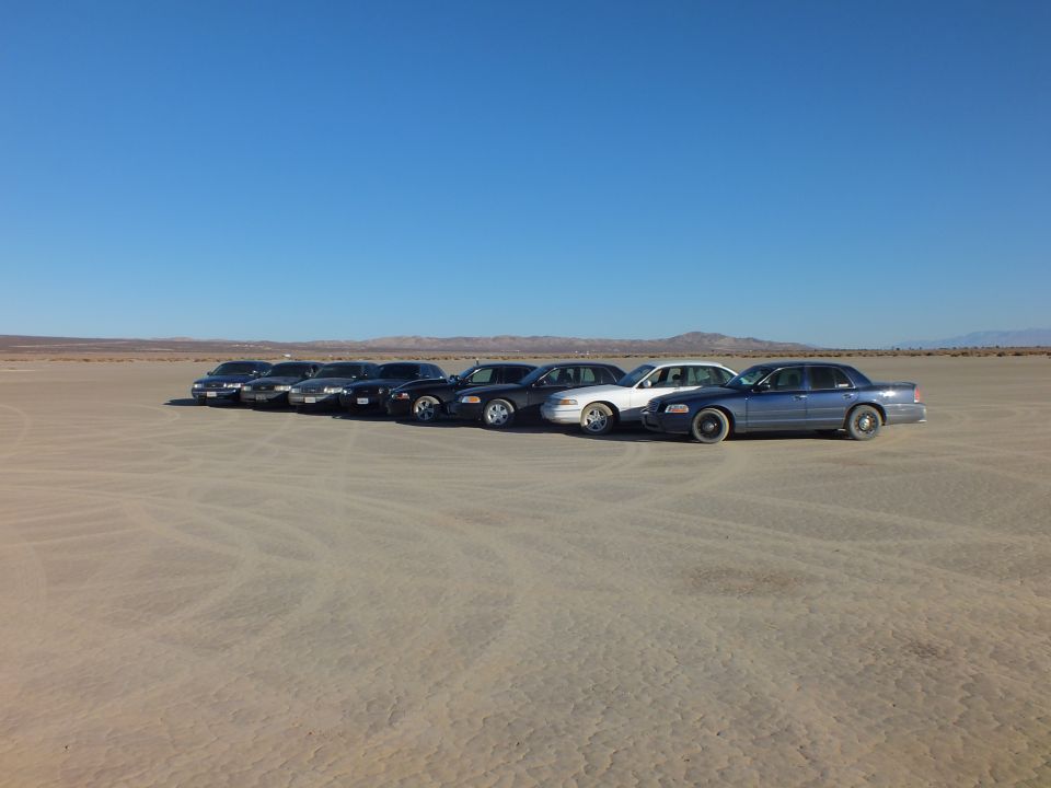 Crown Victoria style sedans angled in a row on dry desert playa