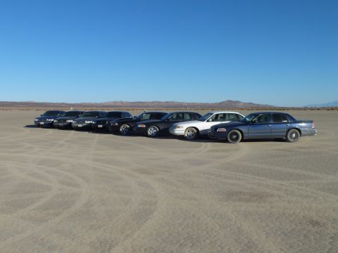 2003 Ford Crown Victoria - Sedan gathering on a dry lakebed with tire marks in the sand