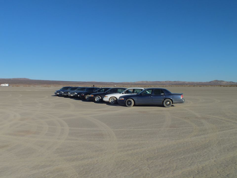 Cluster of full-size sedans parked on an open dry lakebed