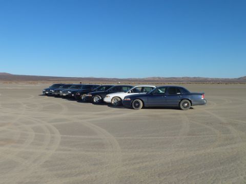 2003 Ford Crown Victoria - Full-size sedans lined up on playa with circular tire tracks in foreground