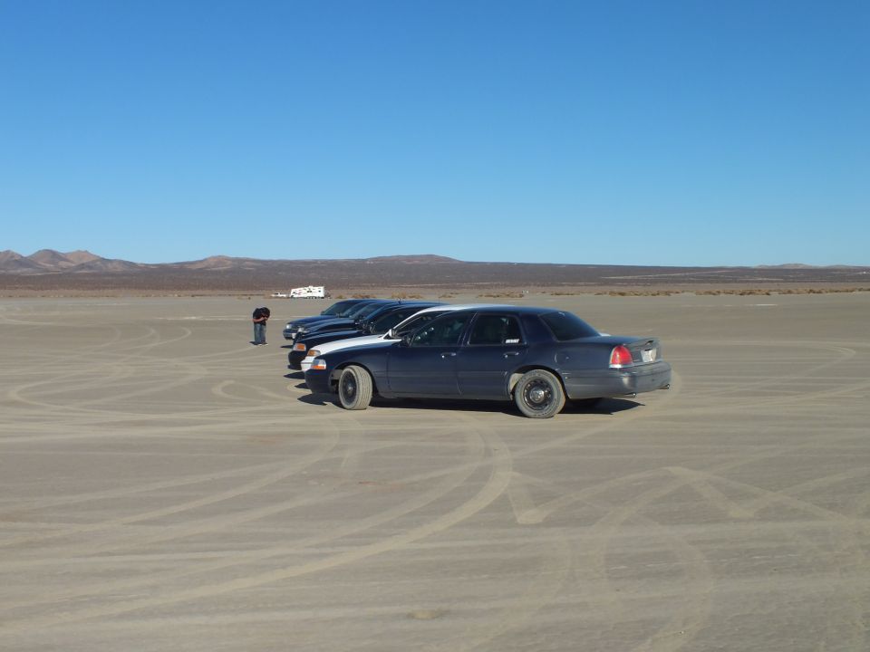 Dark blue Crown Victoria sedan parked side-on on a dry lakebed
