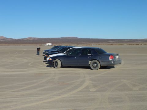 2003 Ford Crown Victoria - Side view of a full-size sedan on playa with vehicles staged in the distance